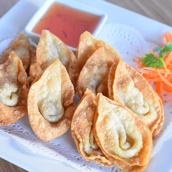 Crispy fried wontons with sweet chili dipping sauce and shredded carrots on a white plate.