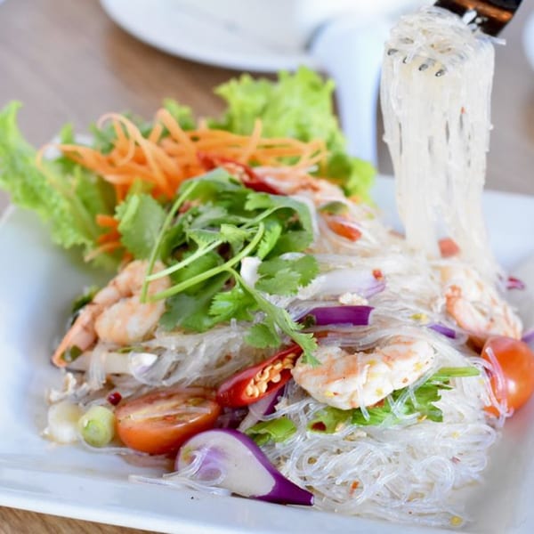 Glass noodles with shrimp, vegetables, and herbs on a white plate, with noodles lifted by a fork.