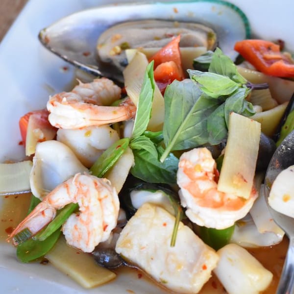 Close-up of a seafood dish with shrimp, mussels, squid, vegetables, and basil on a white plate.