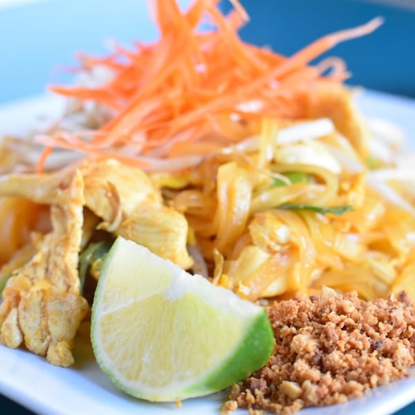 Chicken pad thai with shredded carrots, bean sprouts, a lime wedge, and crushed peanuts.