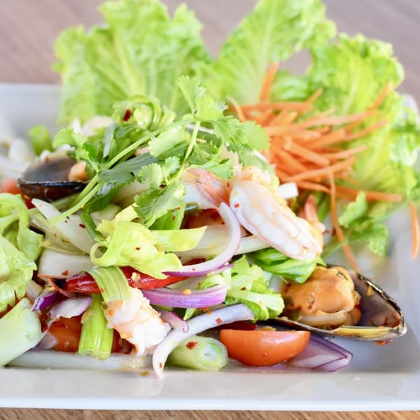 Spicy Thai seafood salad with shrimp, mussels, vegetables, and herbs on a white plate.
